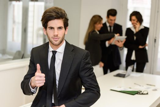 Image of business leader looking at camera in working environment. Man making thumbs up sign