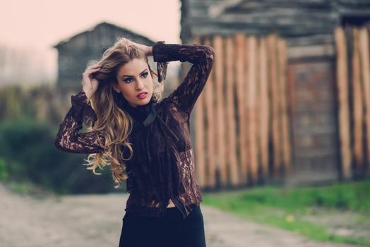 Portrait of blonde young woman playing with her curly hair in a rural road wearing shirt