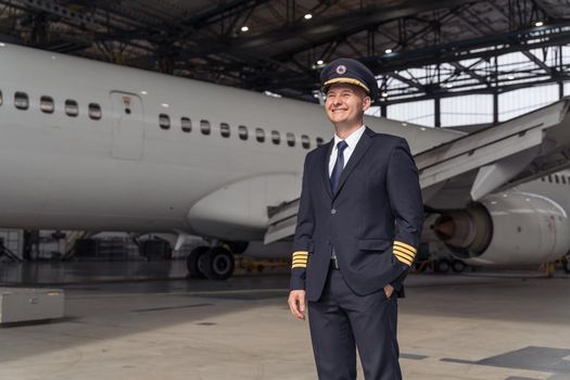 Smiling professional pilot posing against the backdrop of a large white airplane