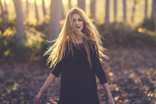 Young blonde woman dancing in poplar forest. Woman wearing black dress with flying hair