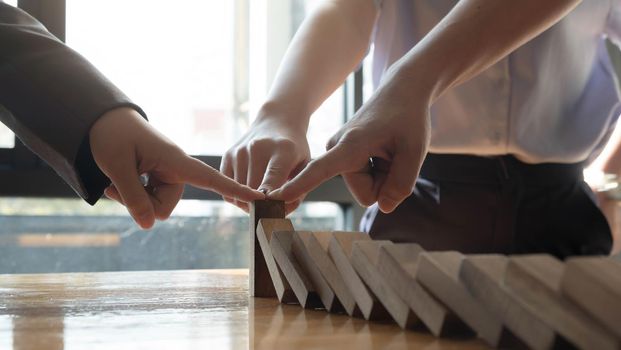 close up team businessman hand stopping falling wooden dominoes effect from continuous toppled or risk, strategy and successful intervention concept for business..