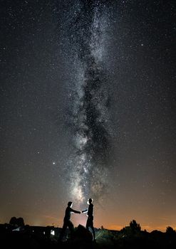 Two persons with masks shaking hands against milky way, vertical composition