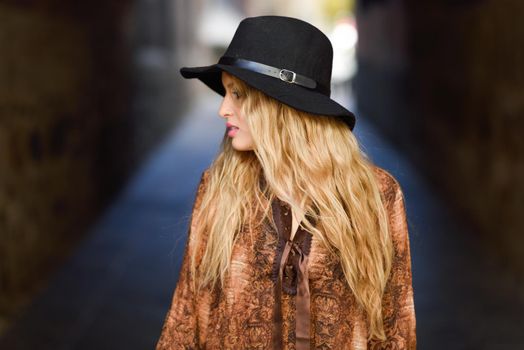 Portrait of beautiful young woman with curly hair. Girl wearing shirt and hat in urban background.