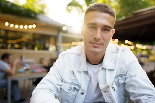 Portrait of a handsome young man sitting in outdoor cafe, close up