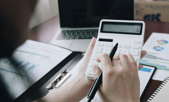 Close up Business woman using calculator and laptop for do math finance on wooden desk in office and business working background, tax, accounting, statistics and analytic research concept.