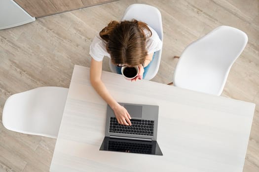 Top view on young Woman working on the laptop in modern place. Home office concept. Girl, laptop, table with coffee cup in modern coworking