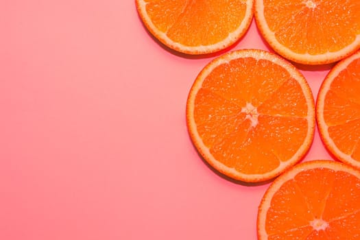 Sliced ripe oranges on a bright pink background.