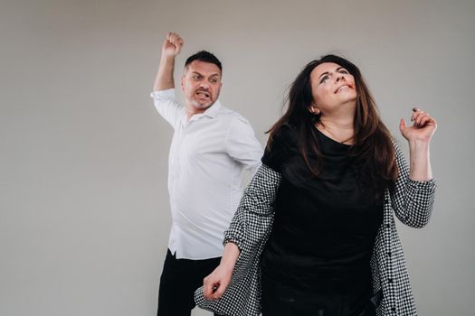 A man swings his fist at a battered woman standing on a gray background. Domestic violence.