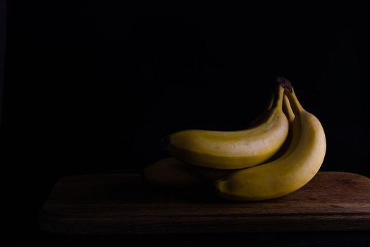 several bananas on a wooden board on a dark background.