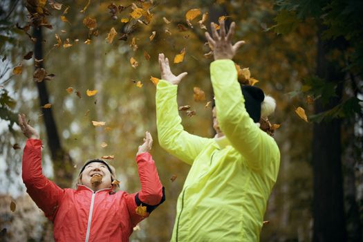 Old women throwing leaves into the air in an autumn park. Mid shot. Day