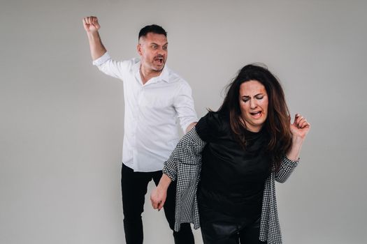 A man swings his fist at a battered woman standing on a gray background. Domestic violence.