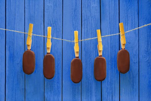 lot of chocolate ice creams hanging on rope near blue background. hot summer dessert and delicious food concept