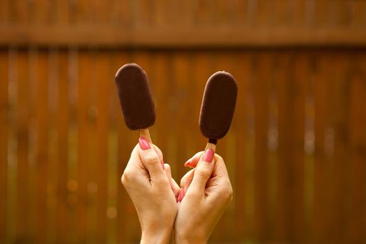 female hands holding two chocolate ice cream on brown background. summer sweet food