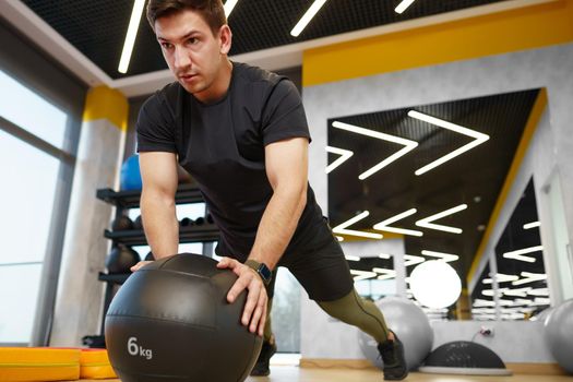 Fit young man exercising with fitness ball in a gym, close up