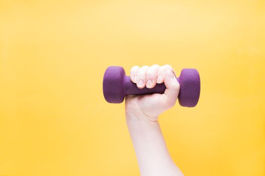 female hand holds a purple dumbbell on a yellow background copy space