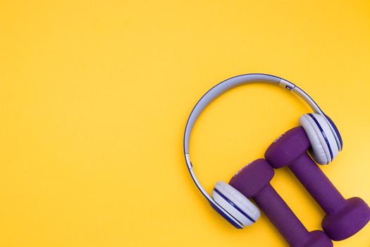 gray and blue headphones and purple dumbbells on a yellow background, copy space, top view, sport and music concept