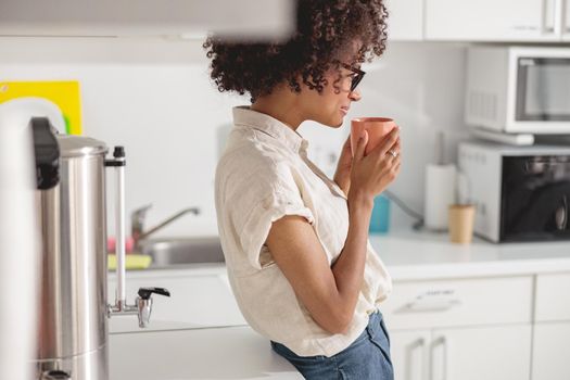 Side view of happy Afro American woman having rest and standing with cup on office kitchen