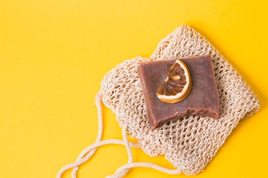 homemade cocoa soap on a knitted washcloth with a slice of dried orange on a yellow background copy space top view