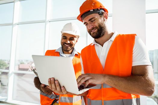 Two specialists supervisors in hardhats using laptop at construction site for work, close up