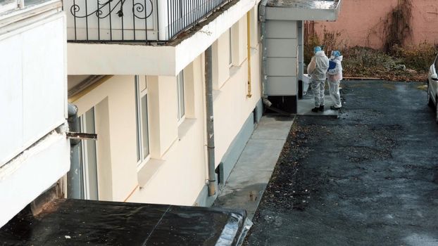 People in white protective anti-virus suits respirators safety goggles and in face shields stand at entrance door upper view