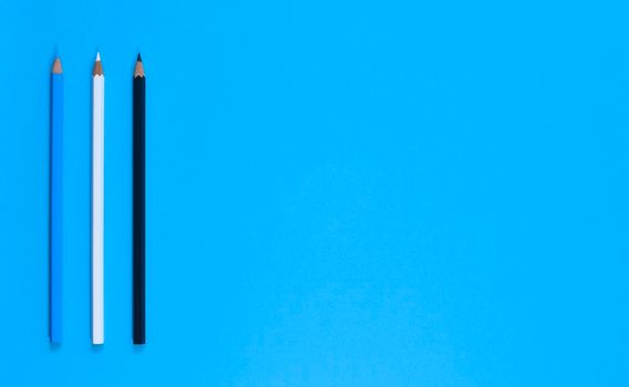 Stationery. Blue, white and black pencil on bright blue background. Top view, flat lay, copy space.