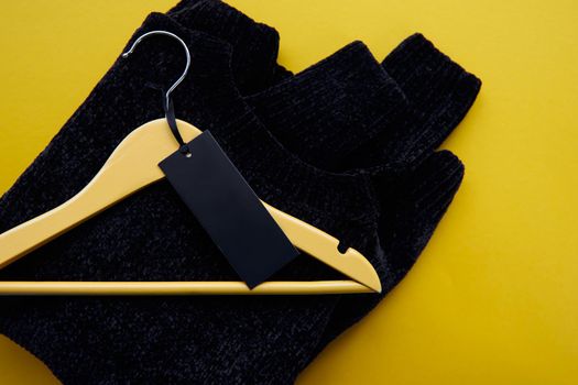 Wooden hanger with black cosy pullover and paper label isolated on yellow paper background. Clothing tag, label blank mockup template, to place your design. Black friday final sale banner.