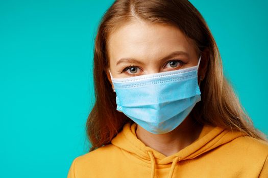 Young beautiful casual woman wearing protective medical mask against blue background