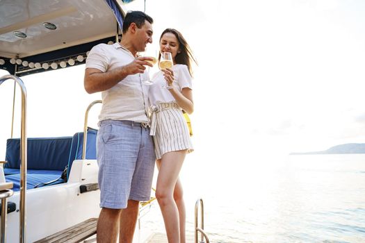 Young loving couple sitting on the yacht deck and drinking wine together