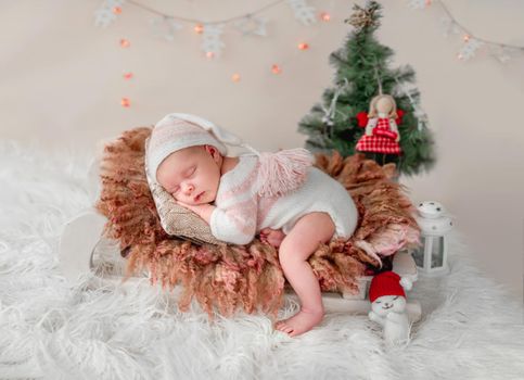 Newborn sleeping on tiny bed next to christmas tree