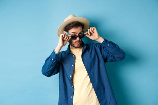 Image of tourist checking out something cool, take-off sunglasses, say wow and looking aside impressed, standing on blue background.