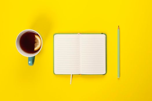 Mint Tea cup and fancy notebook with empty or blank page on bright yellow desk from above, planning and design concept. Top view, flat lay, copy space. Mock up.