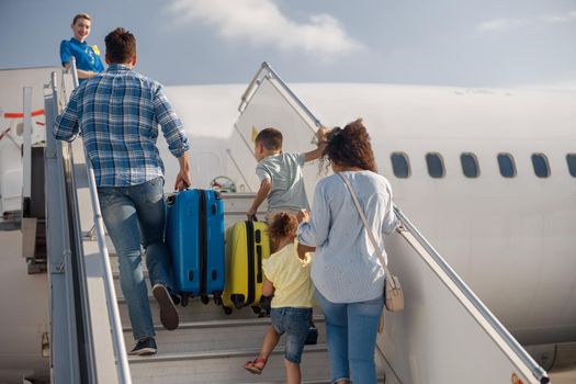 Back view of family of four getting on, boarding the plane on a daytime, ready for summer vacations. People, traveling, vacation concept