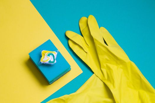 yellow rubber gloves, gel capsules for dishwashers and sponges on a green and yellow background, places of the copy top view, the choice between washing dishes or in the dishwasher