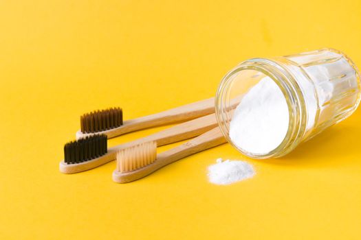 several different bamboo brushes and glass jar with soda on yellow background, copy space, eco friendly lifestyle concept
