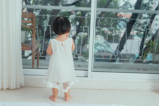 Little cute girl in beautiful dress is sitting near the window at home.