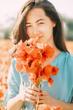 Portrait of smiling beautiful young woman with bouquet of poppies outdoor, looking at camera.