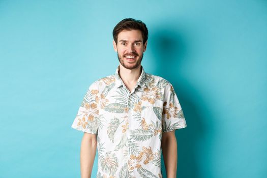 Cheerful caucasian guy going on vacation, wearing summer shirt and smiling, standing on blue background.