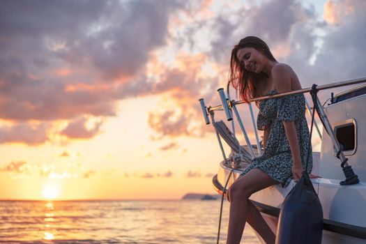 Young attractive woman sitting on the deck of the yacht and enjoying sunset