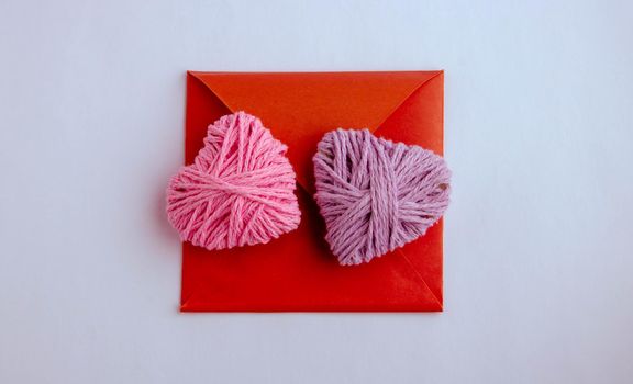 Pink crochet heart in envelope,love concept. Pink and lilac knitting yarn heart shaped. Valentines day minimal concept. Greeting card with heart on a pink background. Top view. Flat lay.