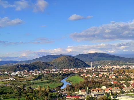 Small european city with small river on low mountains background at bright autumn day