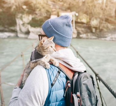 Traveler backpacker young man standing on bridge over river with cute cat.