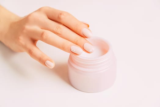 Young female hand using moisturizing cream from jar, concept of beauty and skincare.