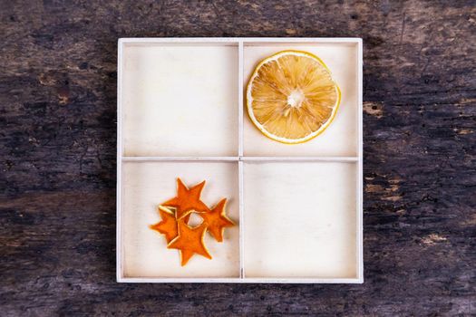 A white box with compartments on a wooden background filled with dried oranges and tangerine stars.