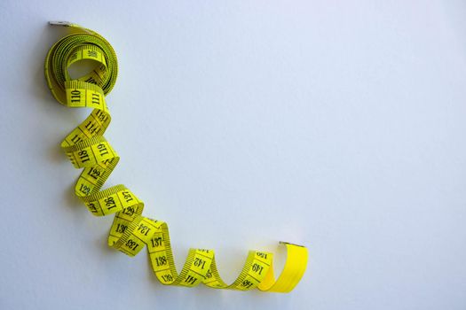 Tape measure in centimetrs as symbol of diet before summer time and healthy lifestyle, tailoring tool on white background.