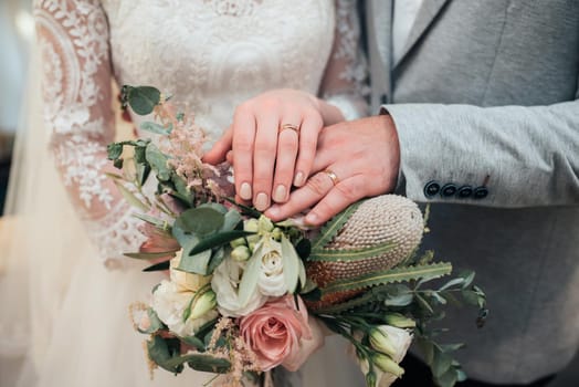 Hands with rings of the bride and groom are lying on the bouquet close-up.