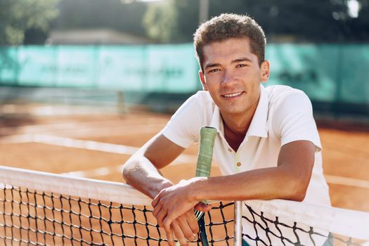 Young mixed race man tennis player with racket standing on tennis court near net