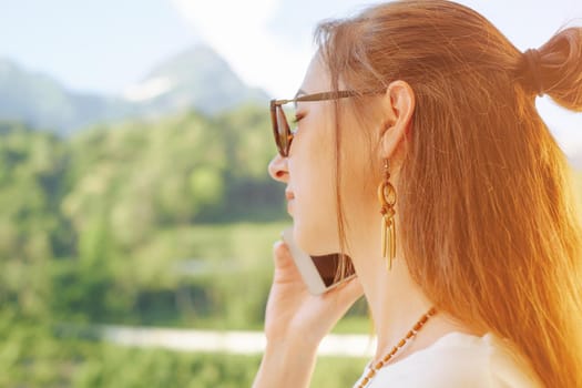Portrait of young woman talking on phone on background of summer mountains.