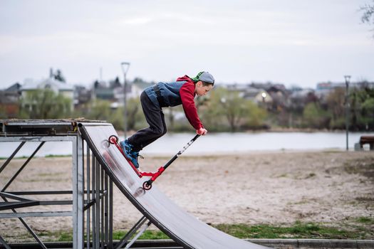 Boy on scooter makes a trick and enjoying his riding in the skate park at cloudy spring day