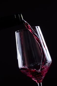 Red wine pouring in wineglass from a bottle on black background. Wine list design menu with copyspace. Alcohol beverage card backdrop.