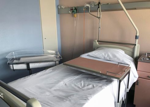 Empty hospital bed for patient and box for newborn baby near the bed